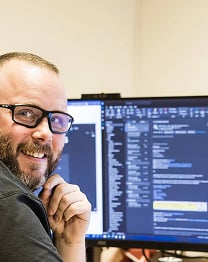 Utvikler smiler foran en dataskjerm med koder i Visual Studio.