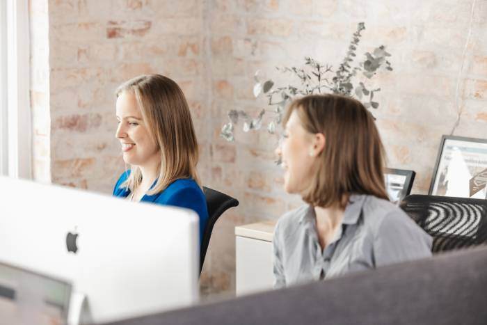 To kollegaer som jobber ved skrivebordet foran dataskjermer i et lyst og inspirerende kontormiljø hos Inbound.